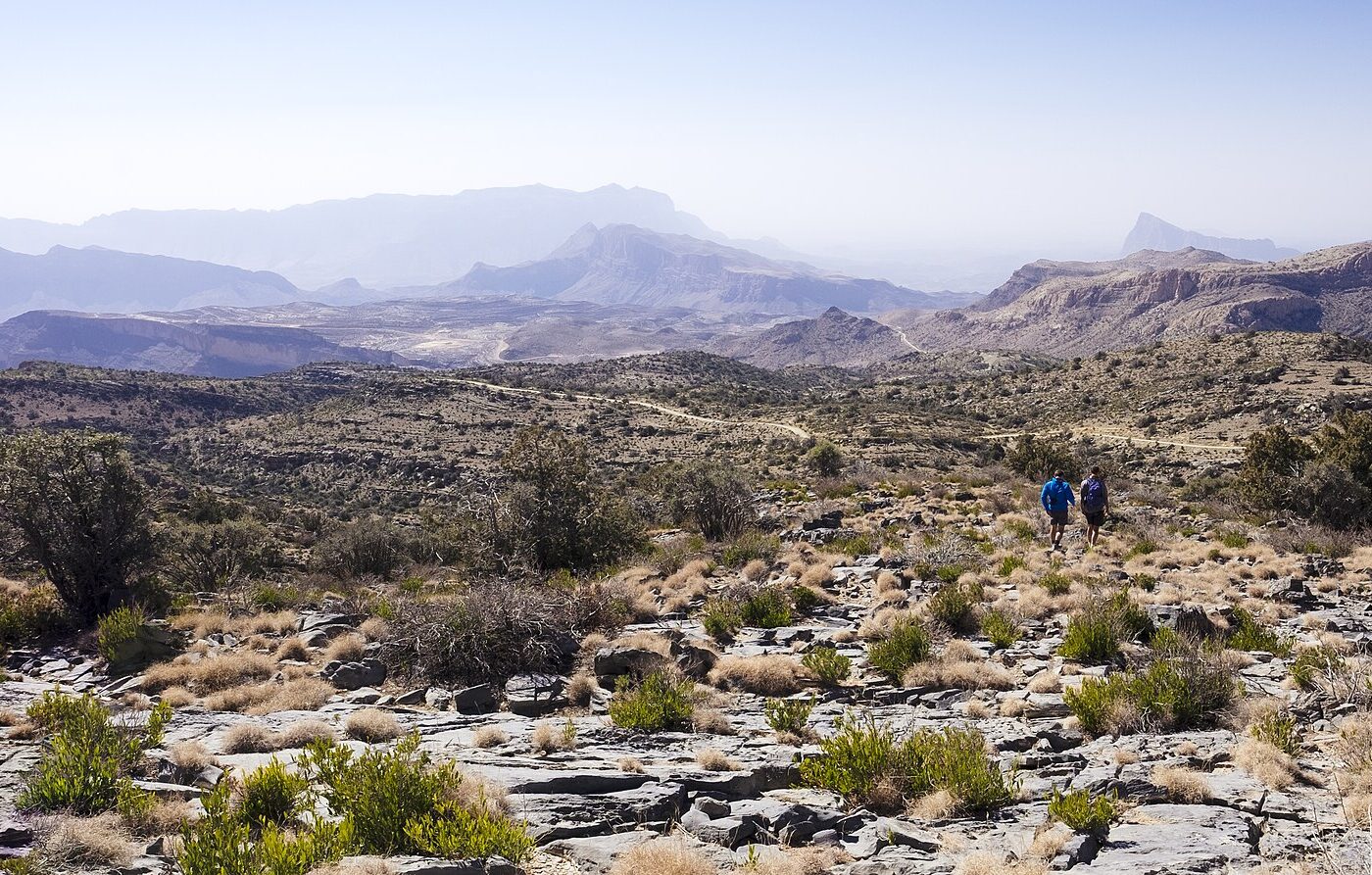 Two walkers on a ridge looking across the Jebel Shams range
